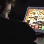 Gambling addicted man with glasses in front of online casino slot machine on laptop computer at night